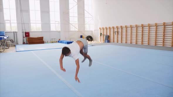 A Teenager Boy is Doing a Cartwheel and a Triple Back Flip in Gym Steadicam alt