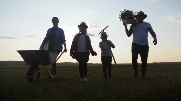 Young Family Having Fun Outdoors in Their Farm, Gardener Woman Pushing Wheelbarrow with Vegetables alt