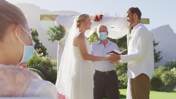 Caucasian bride groom and wedding officiant wearing face mask standing at outdoor altar alt