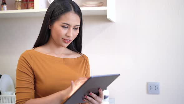 Young woman relaxing standing in kitchen and using digital tablet.