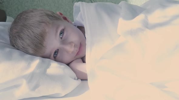 A Little Seven Year Old Caucasian Boy Wakes Up Opens His Eyes and Smiles in a White Bed