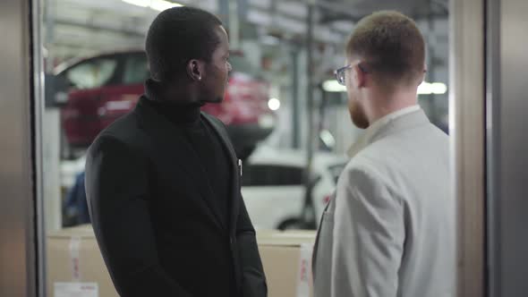 Portrait of Young Handsome African American Man Talking with Car Dealer in Showroom alt