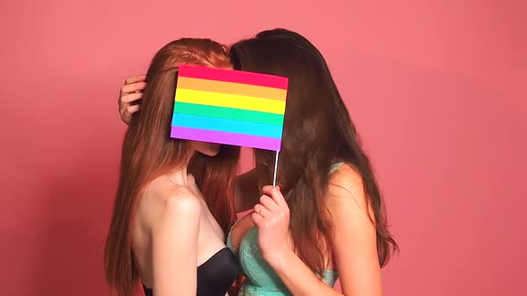 Redhaired Ginger Woman in Pink Studio Background Kissing and Hiding Behind the Rainbow Flag alt