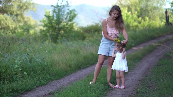 Mom Puts a Wreath of Wildflowers on Her Daughter's Head in Nature alt