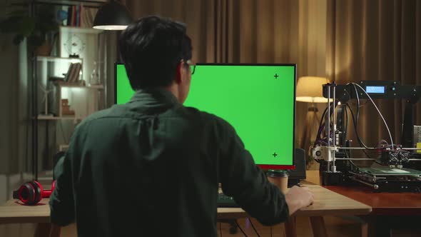 Back View Of Asian Man Work On 3D Printer And Personal Computer With Mock Up Green Screen Display alt