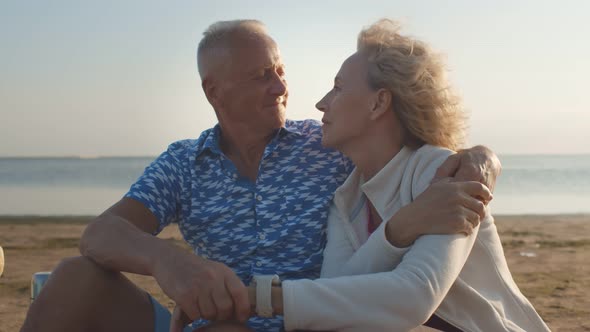 Loving Senior Couple Hugging Looking at Each Other Sitting on Sea Beach Outdoor alt