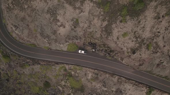 A twisting downward aerial zooming into a parked car on the side of an ancient Hawaiian lava field. alt