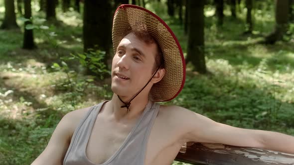 A Guy in a Straw Hat Sits on a Bench in the Woods