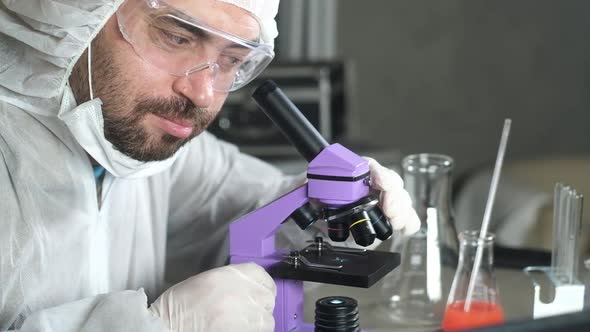 Male scientist in laboratory looking through microscope and change magnification