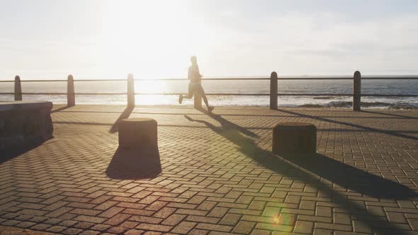 African american woman running on promenade by the sea at sundown alt