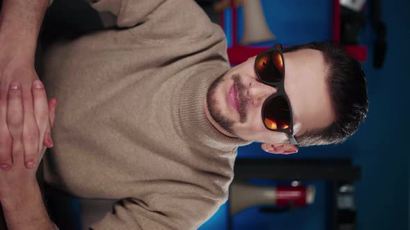 A European Man in Sunglasses Sits at a Table in the Studio and Says Something