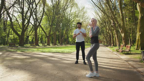 Side View of Attractive Woman in Hijab Drinking Water While Handsome Arabian Guy alt