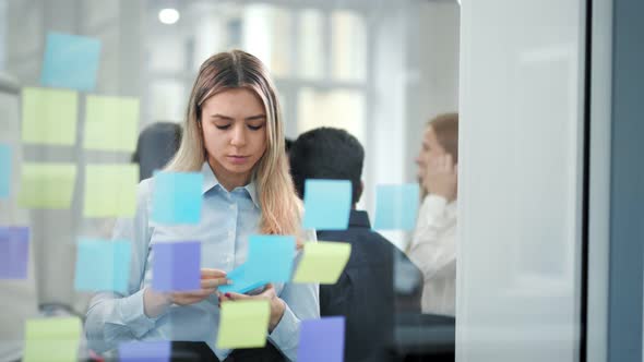 Pensive Female Teamleader Brainstorming Looking at Glass Board with Multicolored Sticky Notes alt