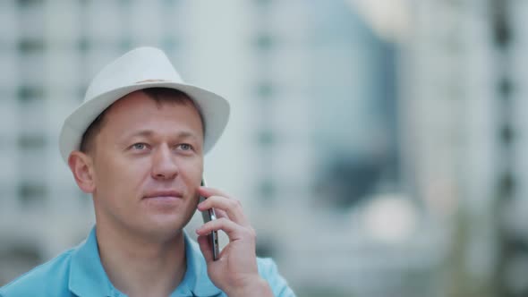 Man in a white hat talking on a mobile phone while standing on a city street tracking camera alt