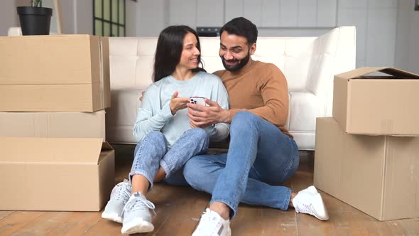 Lovely Indian Couple Choosing New Furniture Online in New House Sitting on the Floor