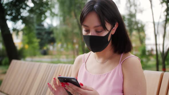 Asian Teenage Girl Wearing Reusable Face Mask Using Smartphone Typing Message Scrolling Watching alt