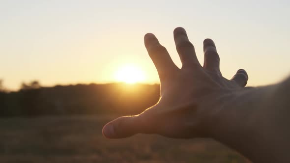 Male Hand Against Sunset. Touch the Sun. Sun Shines Through Fingers. Slow Motion alt