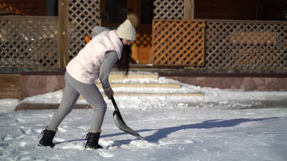 Young Woman Shoveling Snow on Backyard Near the House alt