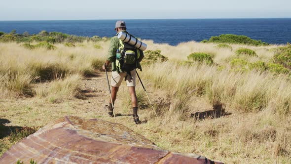 African american man hiking with hiking poles in countryside by the coast alt