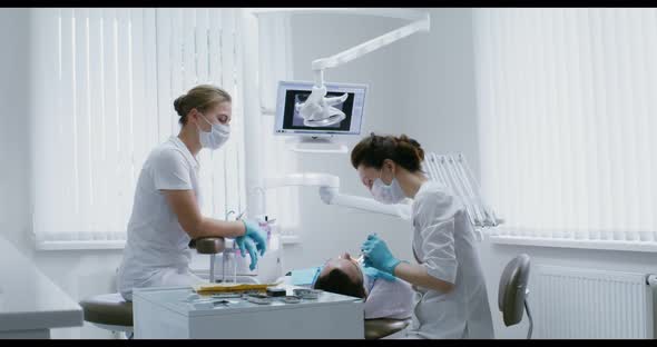 A Female Dentist Examines the Oral Cavity of a Patient Lying on a Dental Chair alt