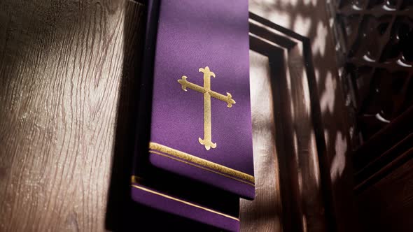 Purple stole with cross lightened by rays of light falling into a confessional. alt