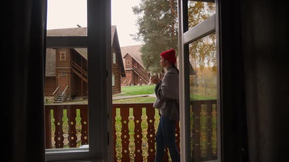 Woman in a Knitted Red Hat and Scarf Drinks Hot Tea Standing alt