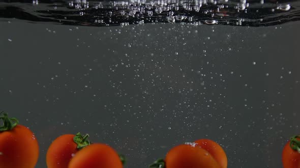 Closeup of Fresh and Health Cherry Tomatoes Falling Into Clear Water with Big Splash on Black alt