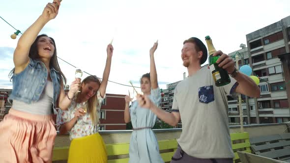 Hipster man and his female friends dancing and playing with firework candles alt
