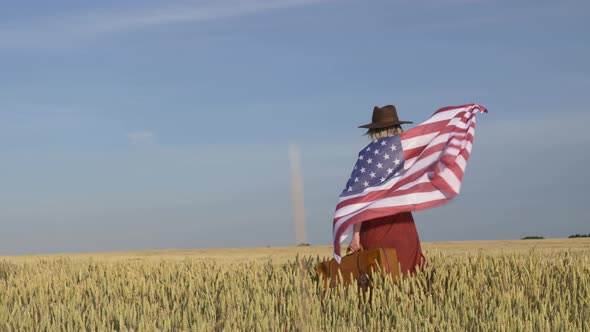 Girl in USA flag with suitcase in wheat field with blue sky on background