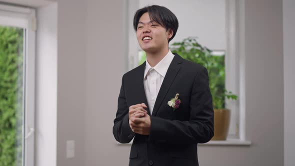 Cheerful Asian Groom with Toothy Smile Showing Victory Gesture Looking Away Laughing alt