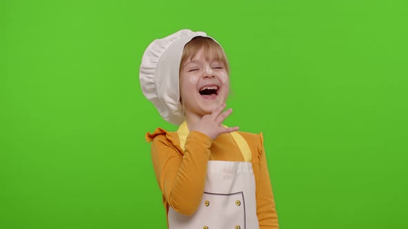 Child Girl Dressed Cook Chef Baker in Apron and Hat Laughing Out Loud After Hearing Funny Joke alt