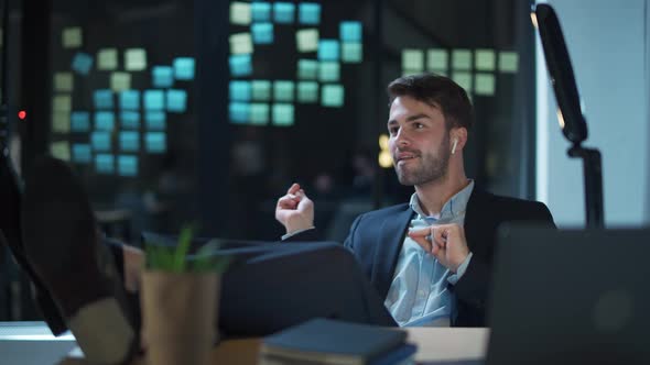 Cheerful Guy Wearing Wireless Headphones Listens To Music in the Workplace in the Office a Good Mood alt