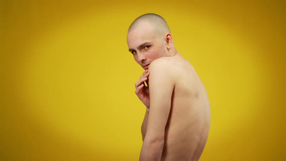 Side View Medium Shot of Young Caucasian Male Queer Looking at Camera Posing at Yellow Background alt