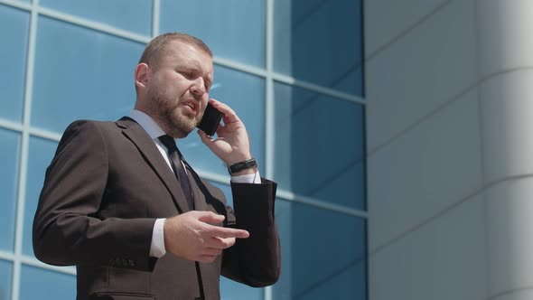 Serious Caucasian businessman talks on phone and gestures, working negotiations. Director of company alt