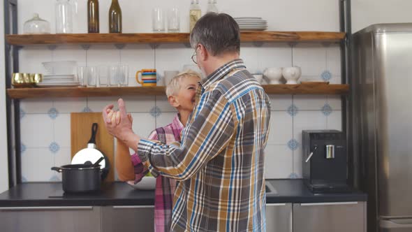 Happy Mature Married Couple Dancing in Kitchen Enjoying Leisure Time alt
