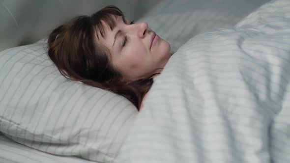 Happy Woman Puts Her Head on a Pillow, Enjoying Going To Bed in a Clean Bed alt