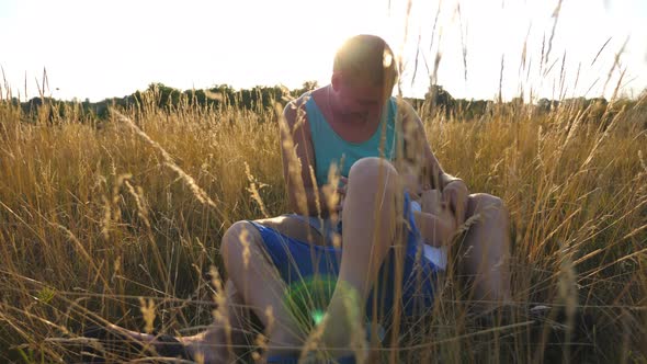 Happy Dad and His Son Sitting on Tall Grass at Field and Having Fun Together on a Sunny Day