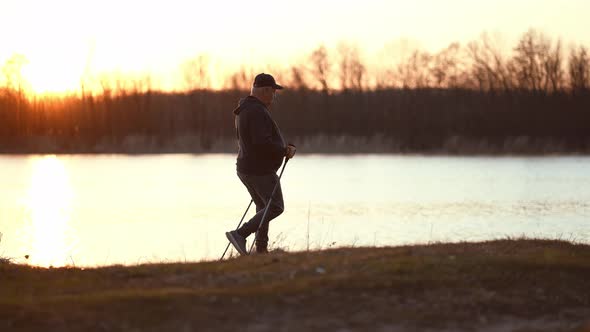 Side View a Man Sport Fitness Nordic Walking with Special Stick on the Ground Next to Water alt