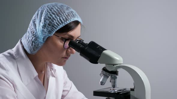 Scientist with Glasses Looks at Sample Through Microscope alt