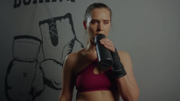A sporty woman in a red tracksuit drinks water in between workouts alt