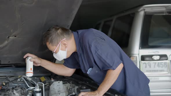 A Senior Male Automotive Mechanic Wearing Face Mask Inspecting The Car Engine In His Shop Bangkok alt