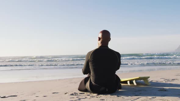Senior african american man sitting with a surfboard at the beach alt