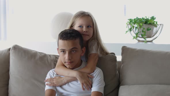 Little Sister and Brother in White T Shirts and Blond Hair Sitting at the Table Sister Hugs Brother