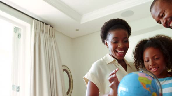 Parents and daughter looking at globe in living room alt