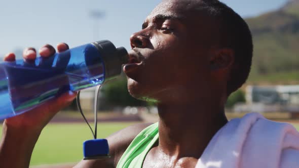 Disabled mixed race man with prosthetic legs sitting on a race track and drinking water alt