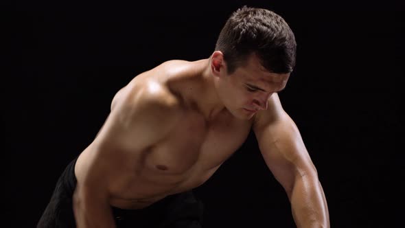 Man Flexes His Hands with Dumbbells Training His Back on a Black Background in the Studio alt