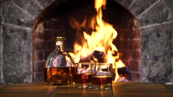 Bottle and Glasses with Whiskey or Cognac on the Background of Fire in the Fireplace alt