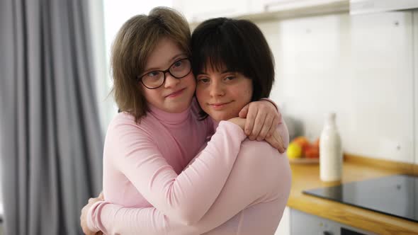 Two Cute Girls with Down Syndrome Standing Together Embracing at Home alt