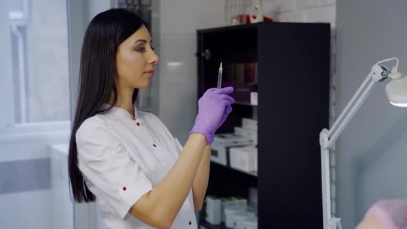 Cute cosmetologist with long hair checks a syringe before the Botox procedure in the office alt