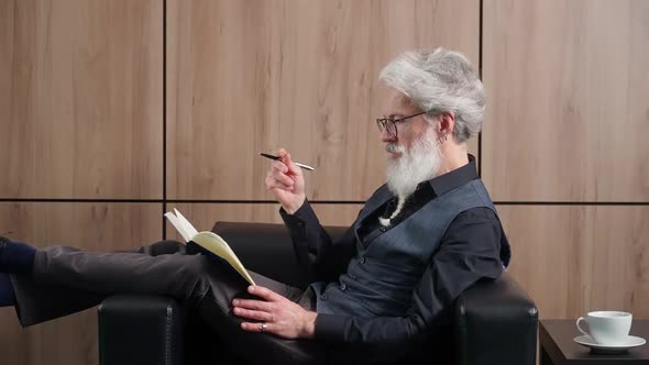 Grayhaired Hipster Man Works in the Office Art Director Writes Down Ideas and Concepts in a Notebook alt